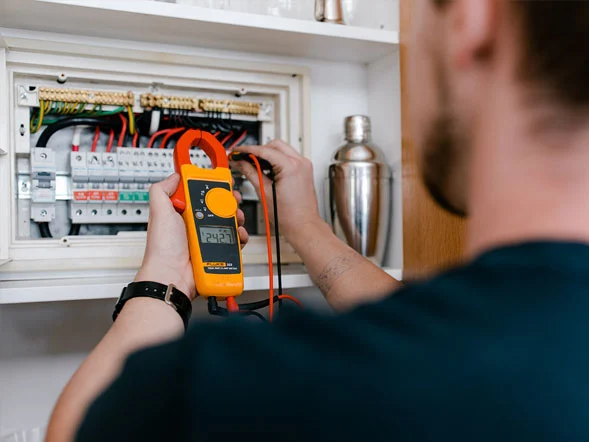 Calibre Connect electrician testing voltage inside a residential switchboard with a clamp meter