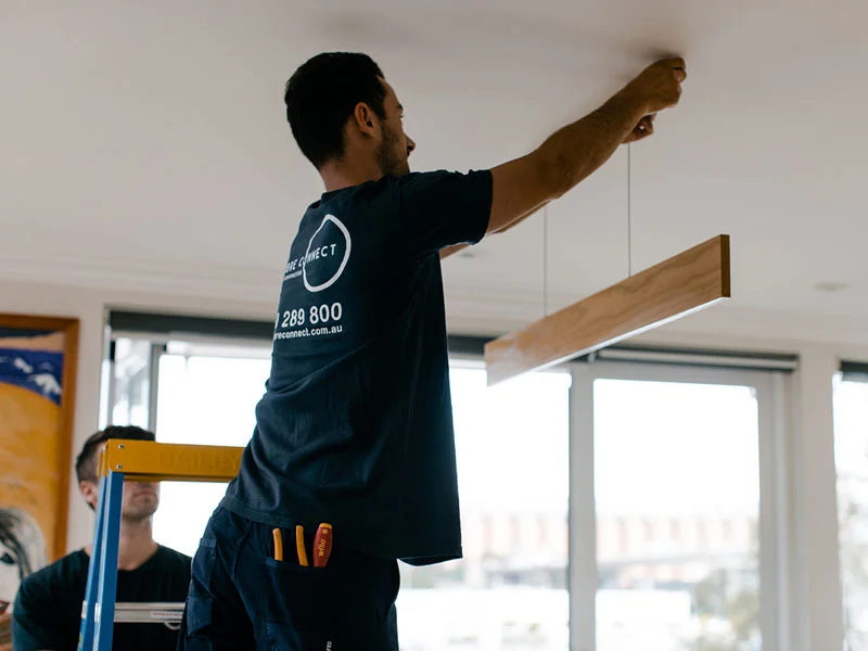 Calibre Connect electrician installing modern timber linear LED pendant light over dining area in Sydney home