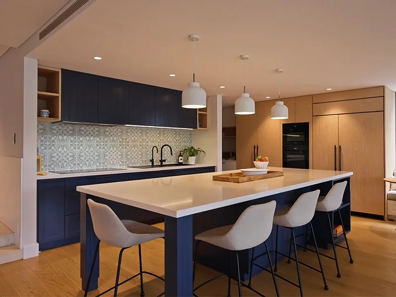 White pendant lights installed above modern kitchen island with blue cabinetry at Wonga Road, Cremorne