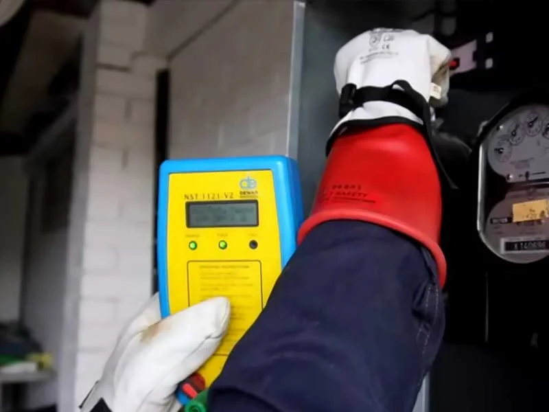 Level 2 electrician testing a three-phase mains switchboard with insulated gloves after main switch and SPD upgrade