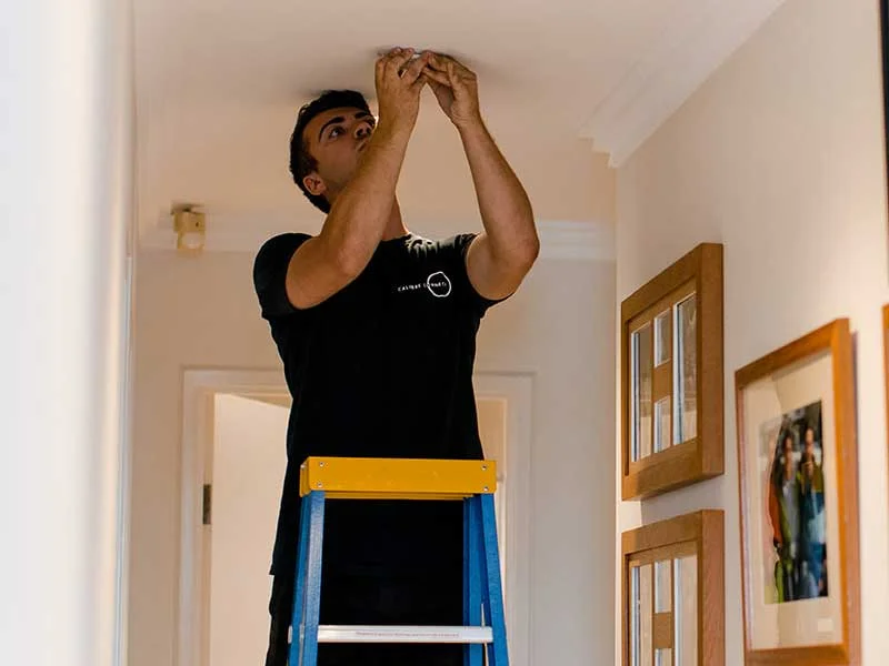 Calibre Connect electrician installing a photoelectric smoke alarm on a ceiling in a Sydney home