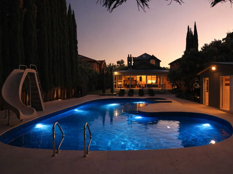 Backyard swimming pool at dusk with installed underwater LED pool lights illuminating the water naturally