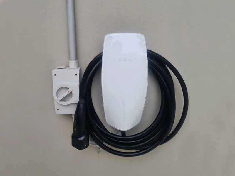 Tesla Wall Connector EV charger mounted on exterior wall with charging cable and isolator switch