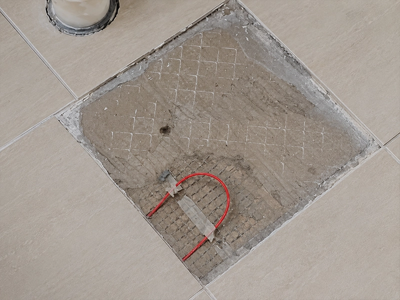 Damaged electric underfloor heating cable exposed beneath floor tiles during repair work in Sydney