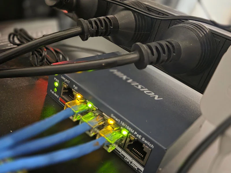 Active Hikvision 4-port Smart PoE Switch (DS-3E1105P-EI) terminated with blue data cables in a home network comms rack.