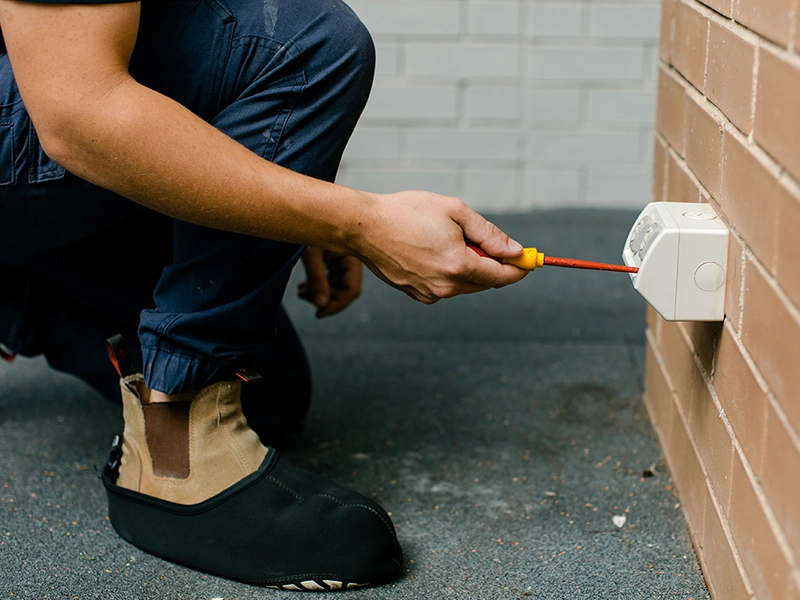 Electrician installing a weatherproof outdoor power point on a brick wall in Sydney
